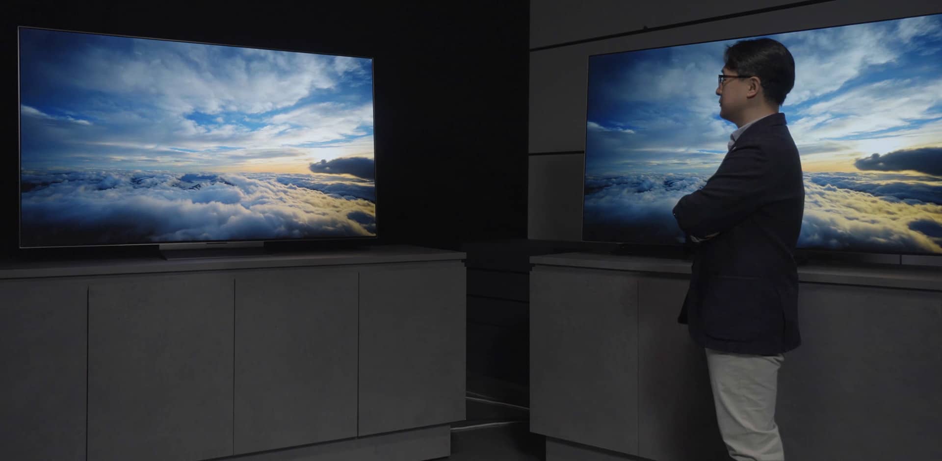 Mr.Kim is looking at two META Technology OLED displays with his arms crossed, and a cloudy sky image is visible on the screen.