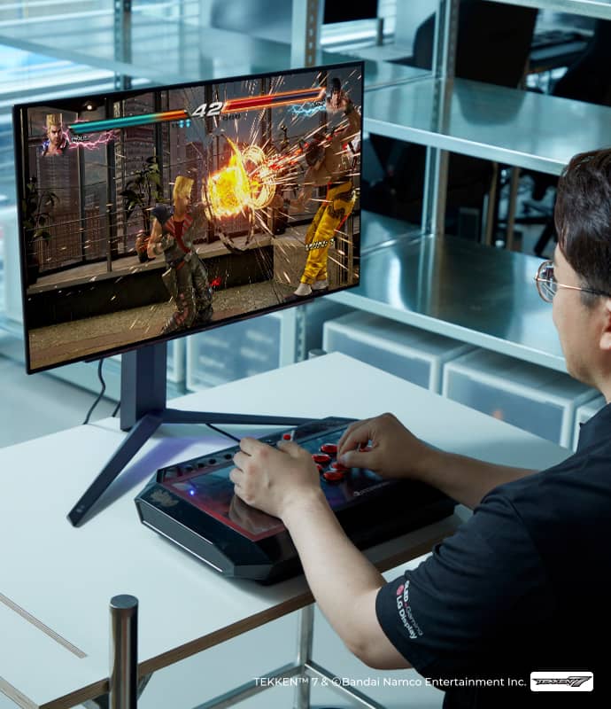 DRX 무릎이 게이밍 OLED 모니터를 보며 철권 게임을 하고 있고, 화면에는 격투 장면이 보인다.